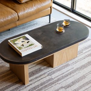 Oval pill-shaped coffee table with coffee shell finish and maple wood base styled with ceramic accessories